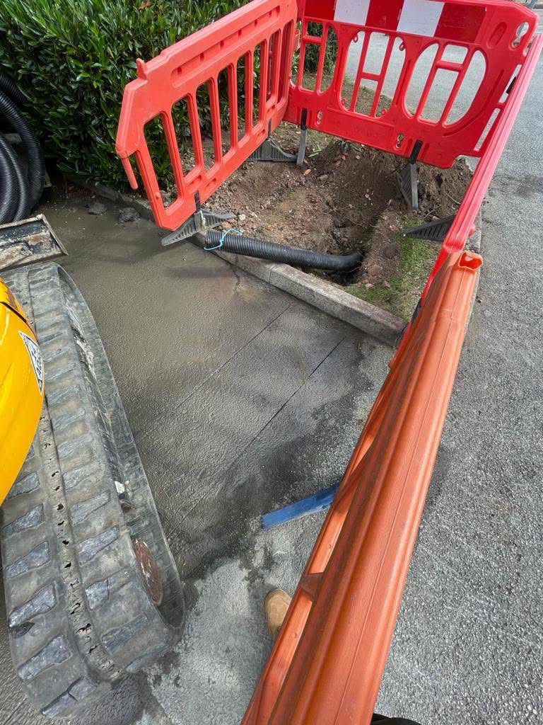 Excavator beside a fresh concrete pour with drainage pipe and safety barriers